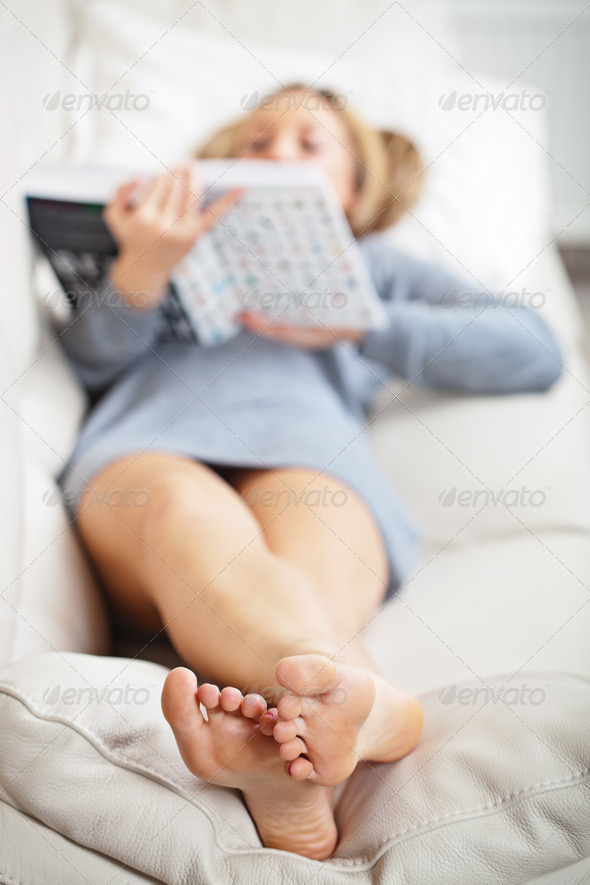 Woman lying on sofa with book