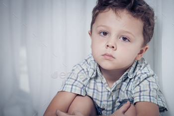Photodune Portrait of sad little boy sitting near the window at home 18788073