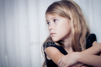 Photodune Portrait of sad little girl sitting near the window at home 18788074