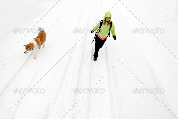 Woman hiking with dog on winter road and snow