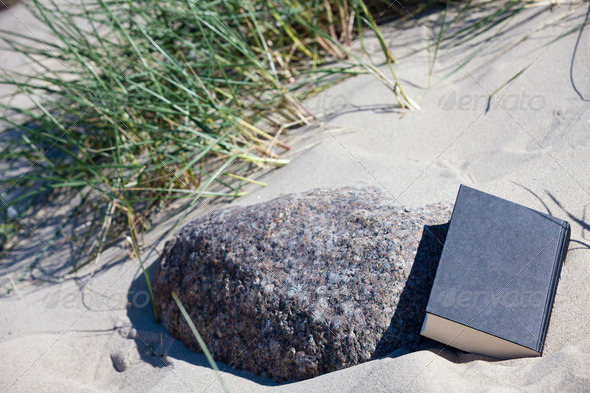 A closed book lies in the sand at a stone