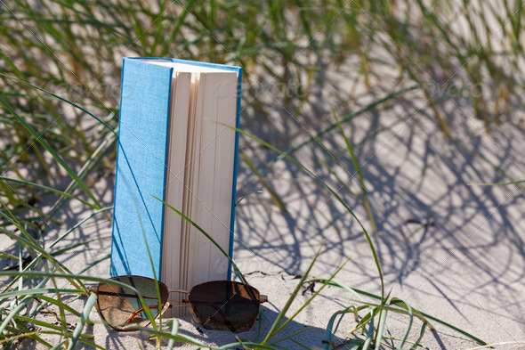 A book with a sunglass lying in the sand in a dune