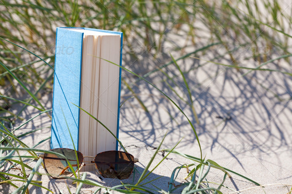 A book with a sunglass lying in the sand in a dune
