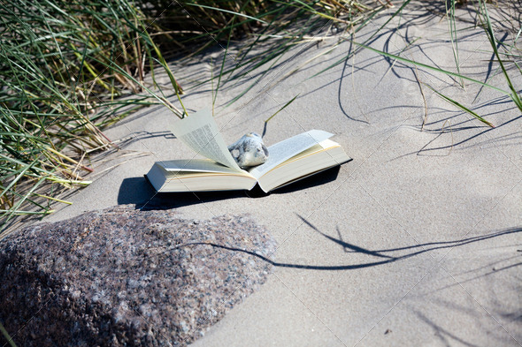 Read on the beach. Book lies open on the sandy beach between the dune grass
