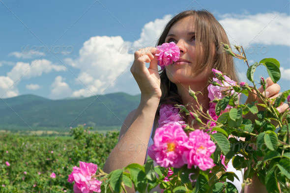 Beautiful girl smelling a rose in a rose field