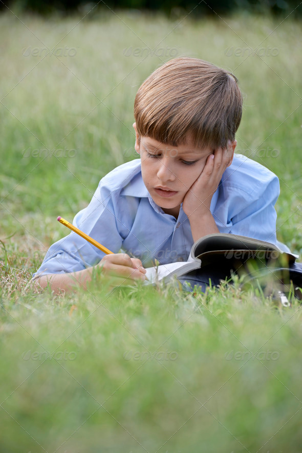 Young school boy doing homework alone, lying on grass - Stock Photo - Images
