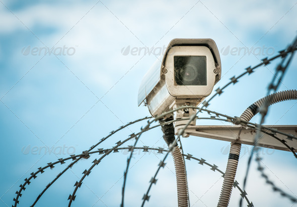 Observation camera and barbwire on blue sky.