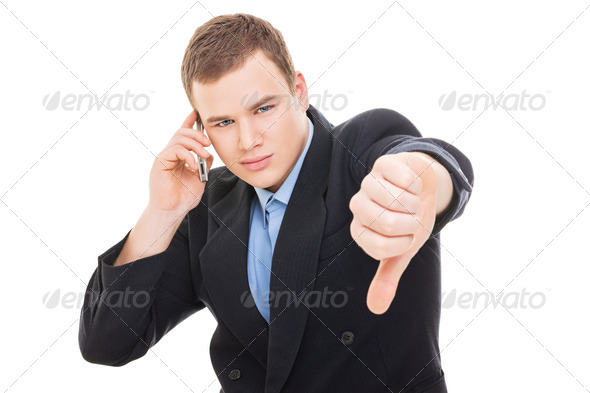 Young businessman speaking on smartphone showing thumb down - Stock Photo - Images