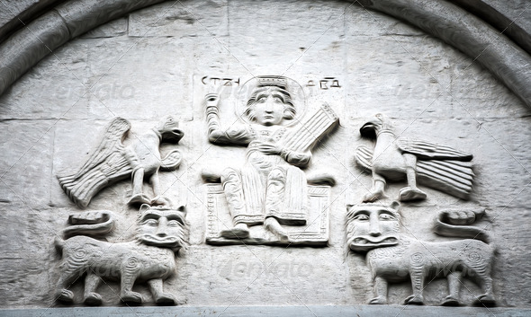 Arched wall in church with five carved characters.