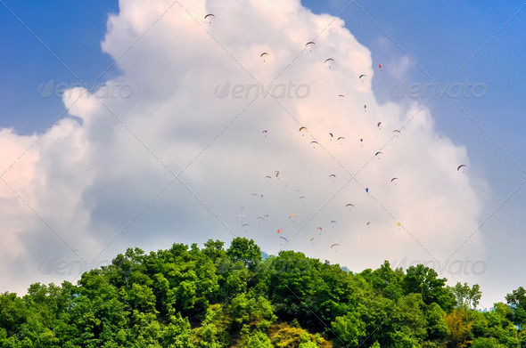 Many parachutists paragliding above green mountain