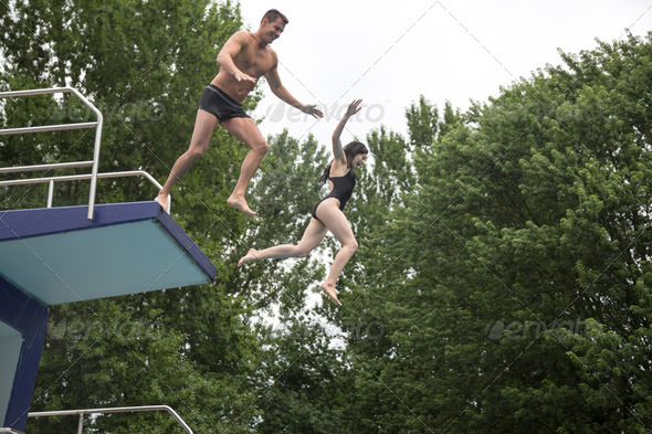 Couple jumping from a diving board into a swimming pool