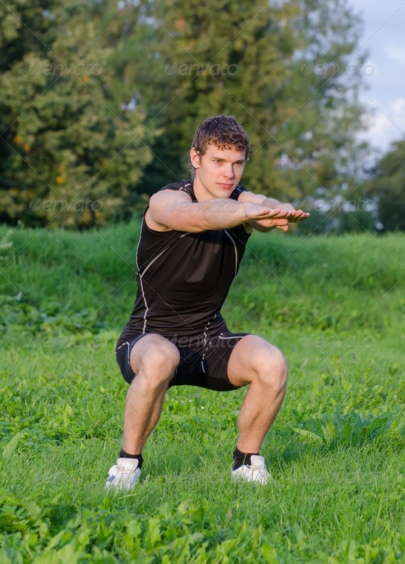 Young sportsman crouches before workout in park - Stock Photo - Images