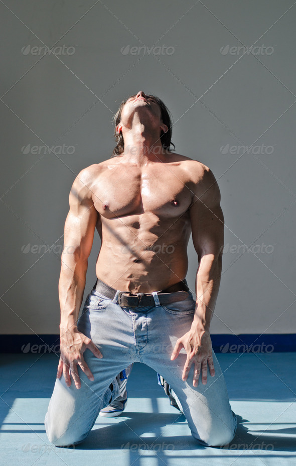 Attractive young man with muscular body, kneeling and looking up