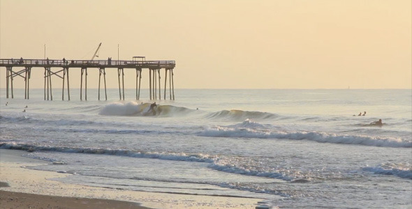 Surfers Catching Waves Near Pier at Sunrise Surfers Catching Waves Near Pier at Sunrise