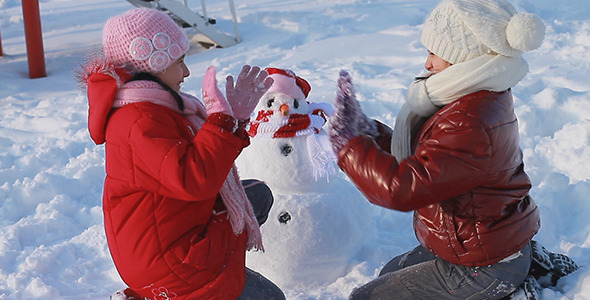 Happy Girls Playing a Game in Front of a Snowman Happy Girls Playing a Game in Front of a Snowman