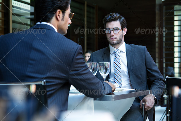 Two smiling business men have dinner at restaurant