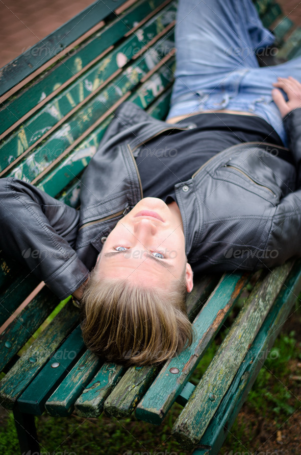 Handsome blond young man laying on park bench