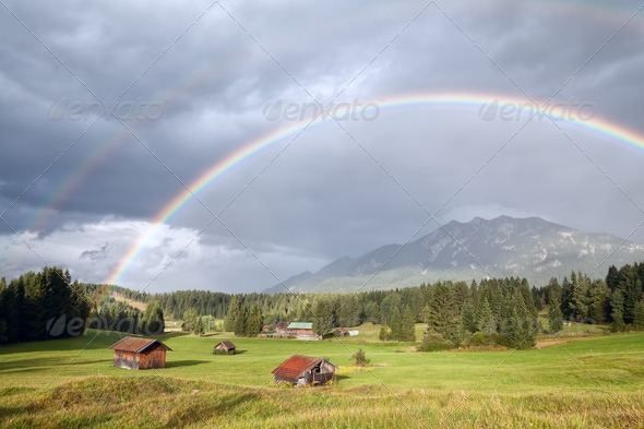 colorful rainbow over alpine meadows with wooden huts