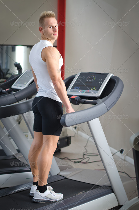 Blond young man standing on treadmill