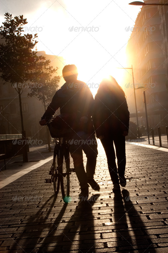 Young couple walking down the street with a bicycle at sunset.