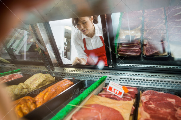 Saleswoman Looking At Variety Of Meat Displayed In Shop