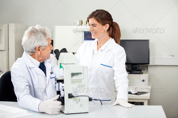 Scientist Discussing With Colleague While Using Microscope
