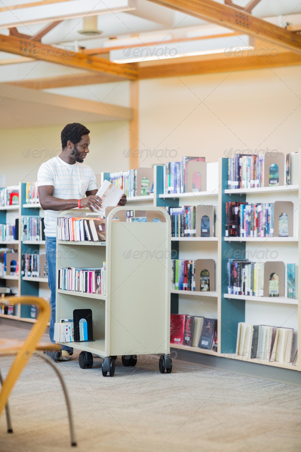 Librarian With Trolley Arranging Books In Library