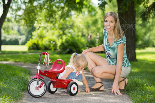 Mother With Daughter Crouching By Tricycle On Walkway