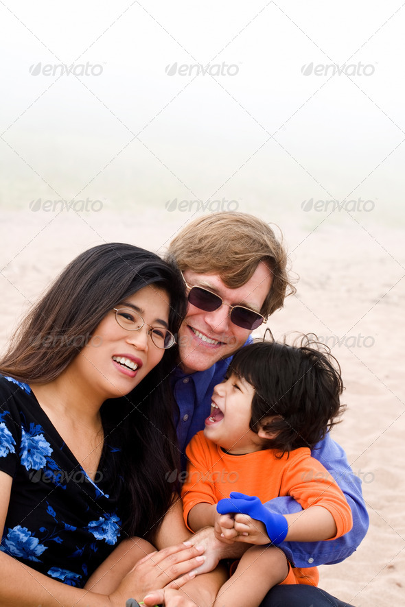 Mutiracial family with disabled son sitting on beach on misty day.