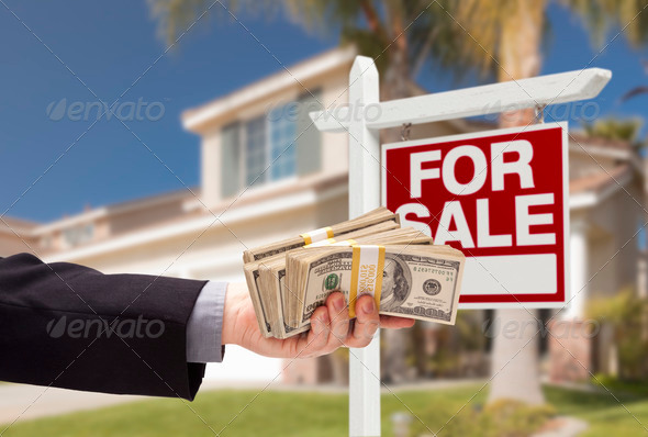 Buyer Handing Over Cash for House with Home and For Sale Real Estate Sign Behind.