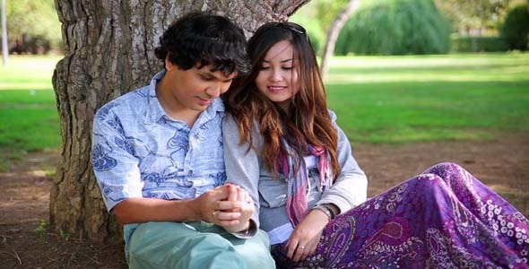 Young Couple Relaxing Against Tree In A City Park Young Couple Relaxing Against Tree In A City Park