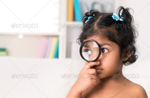 Cute Indian girl peeking through magnifying glass.