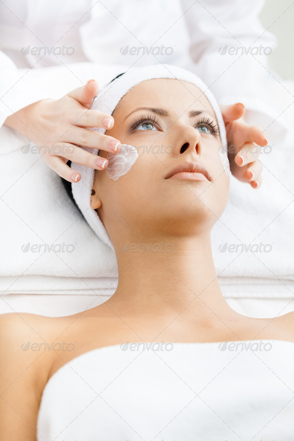 Hands of therapist apply cream to woman face