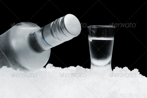 Bottle with glass of vodka lying on ice on black background