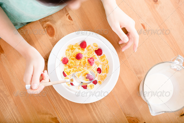Top view of girl eating cereals with strawberry and milk