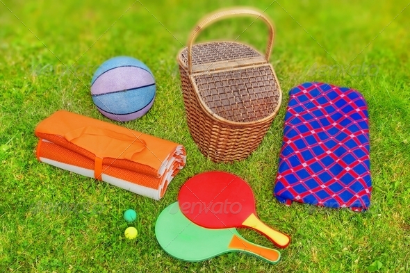 Picnic basket, blanket, racquetball and ball in the grass