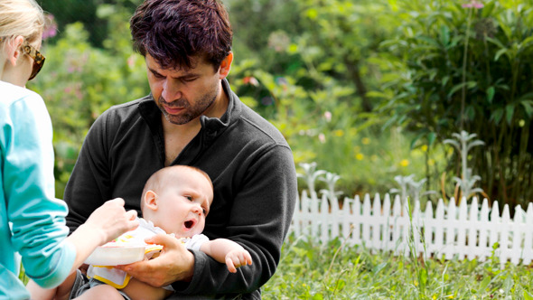 Parents Feeding Baby Sitting On The Grass Parents Feeding Baby Sitting On The Grass