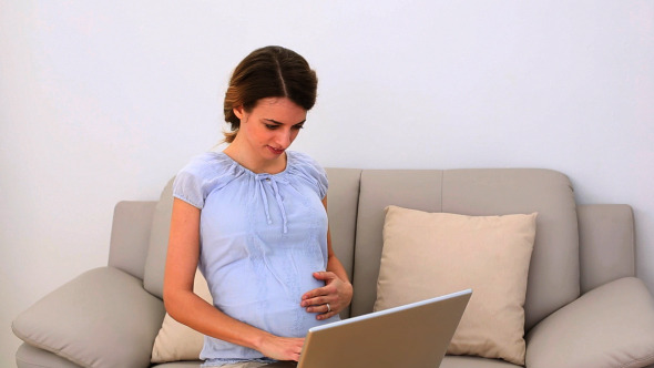 Pregnant Woman Using Her Laptop On The Couch Pregnant Woman Using Her Laptop On The Couch
