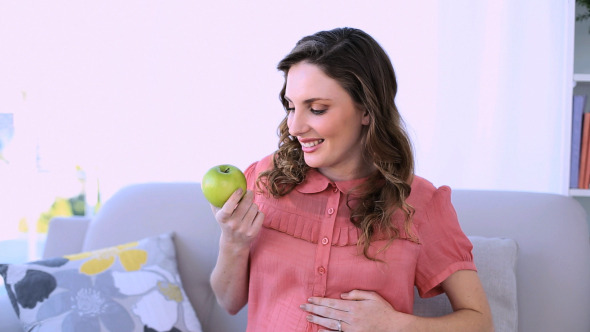 Pretty Pregnant Model Sitting Holding A Apple