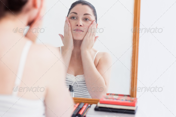 Young woman applying cream on face while looking at mirror (Misc) Photo Download