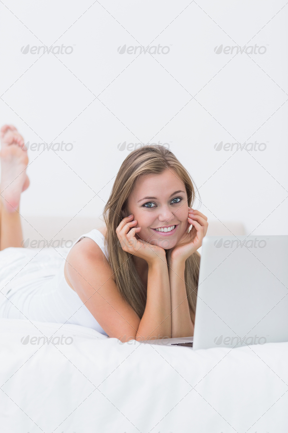 Blonde woman lying on the bed with her laptop on the bed in the white bedroom (Misc) Photo Download