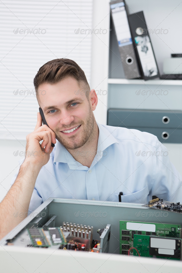 Portrait of young smiling computer engineer on call in front of open cpu at workplace (Misc) Photo Download