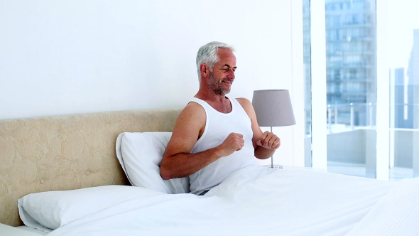 Smiling Man Yawning And Stretching Sitting On Bed Smiling Man Yawning And Stretching Sitting On Bed