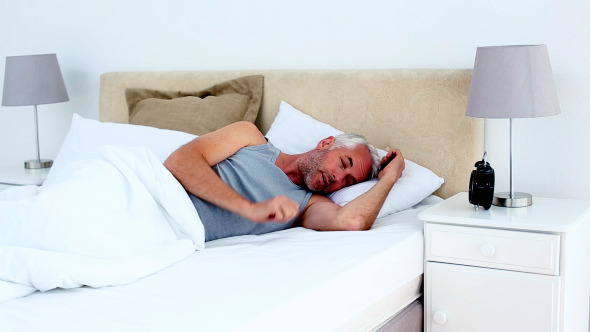 Groggy Man Waking Up And Looking At Alarm Clock Groggy Man Waking Up And Looking At Alarm Clock