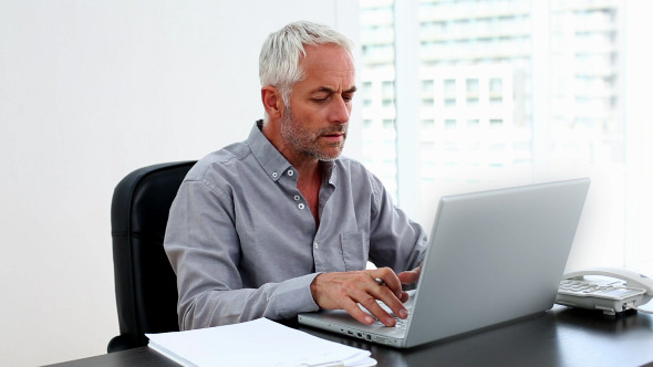 Casual Businessman Working On Laptop At Desk Casual Businessman Working On Laptop At Desk
