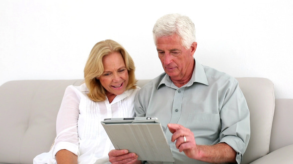Retired Couple Using Their Tablet On The Couch Retired Couple Using Their Tablet On The Couch