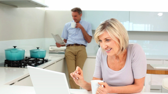 Woman Using Laptop While Her Husband Is Standing Woman Using Laptop While Her Husband Is Standing